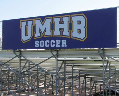UMHB Wayfinding Large sign attached to fencing behind stadium bleachers